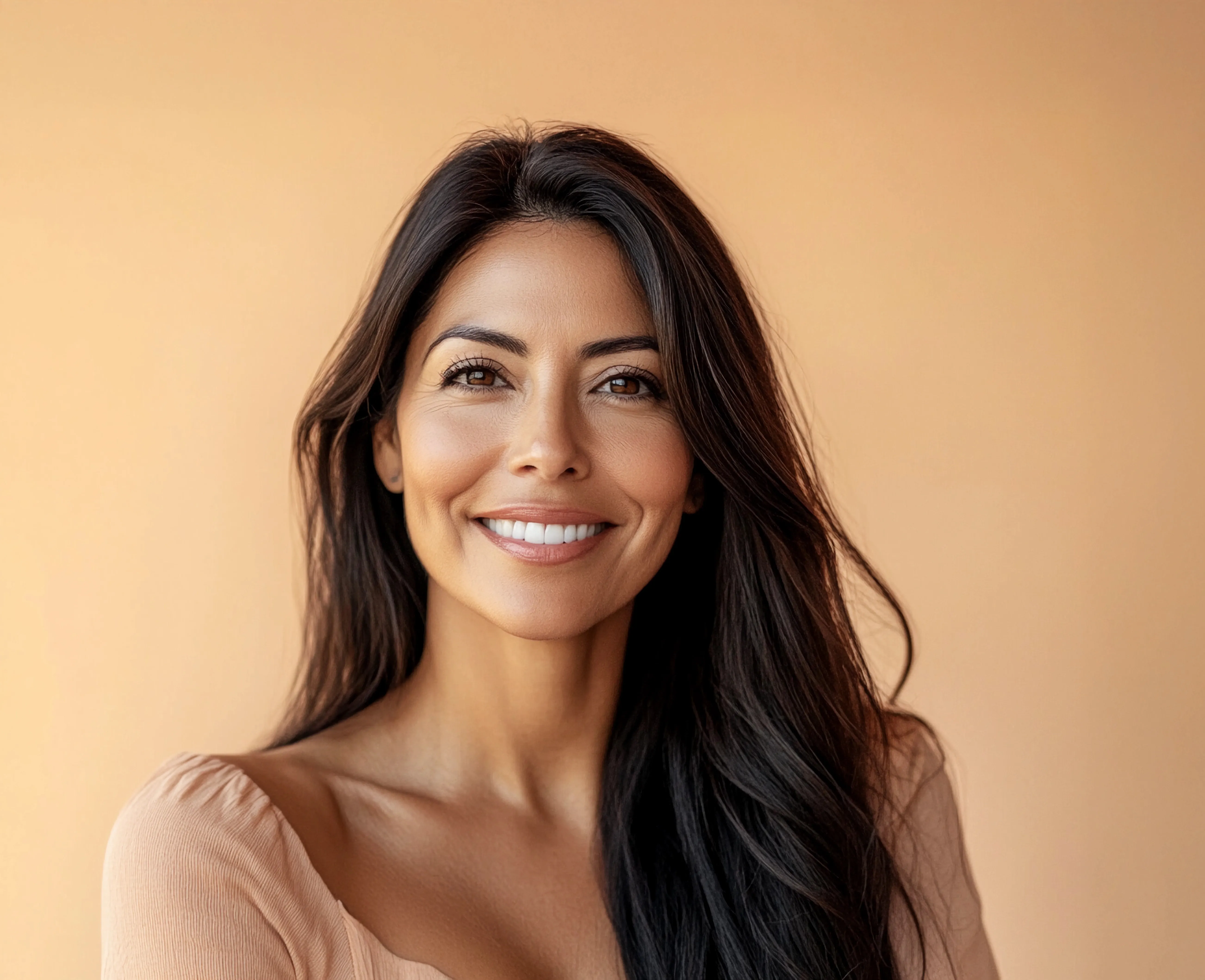 A smiling woman with long dark hair against a warm peach background